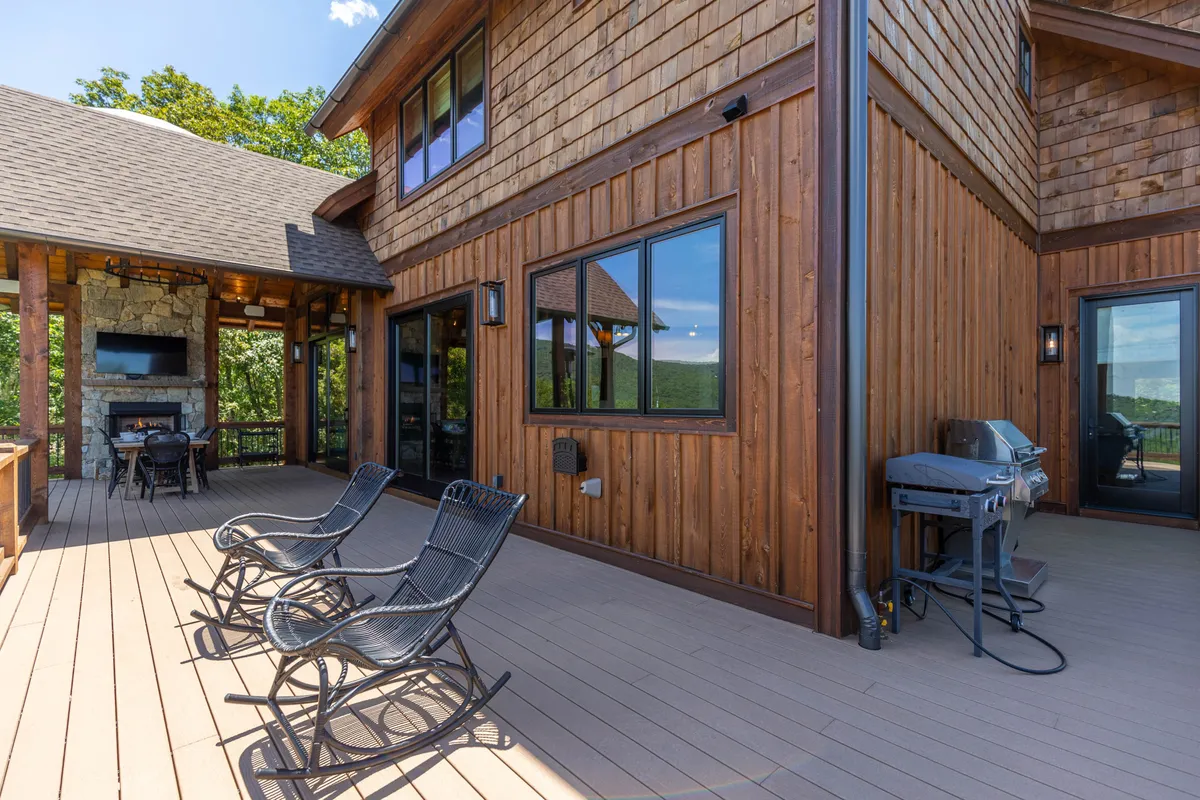 A spacious wooden deck with an outdoor rock fireplace, comfortable seating, a grill, and sweeping mountain views. The area is designed for relaxation, socializing, dining outdoors, and enjoying the natural surroundings.