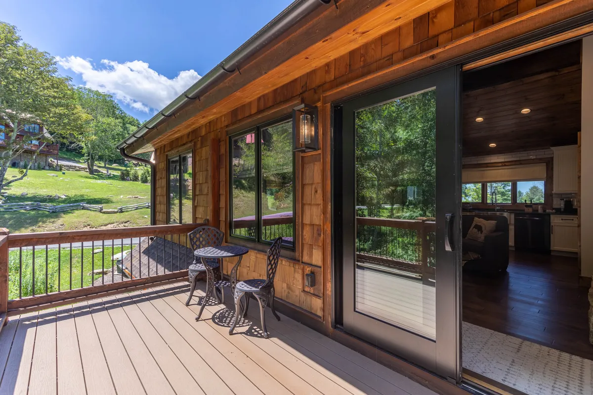 An outdoor seating area on a wooden deck overlooking a landscaped yard, framed by large windows of the house. The setup suggests a peaceful spot for group conversations, stargazing, or morning coffee while connecting with nature just outside the lodge.
