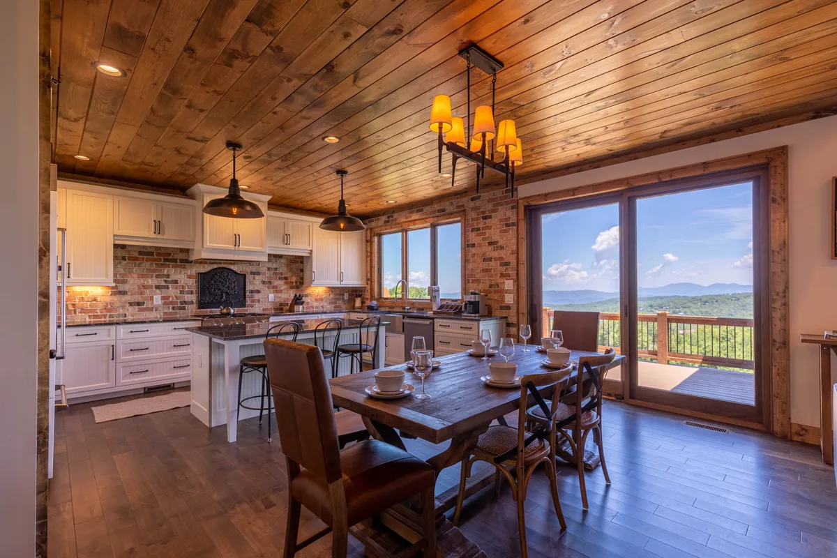 A stylish dining area is shown here, with a large table set against windows offering mountain views. The kitchen island is also visible, connecting the dining and kitchen spaces and highlighting the open-concept layout.