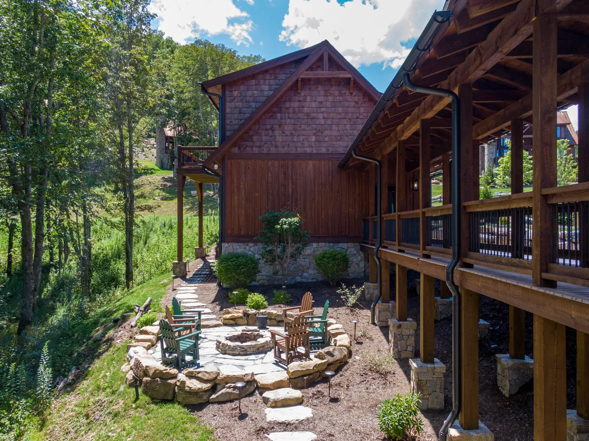 This inviting fire pit area includes a circular stone fire pit surrounded by wooden seating nestled in lush greenery. The tranquil setting suggests relaxed evenings making s’mores, sharing stories, or stargazing under the open sky.