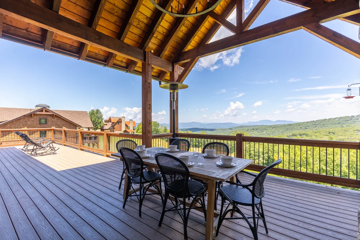 An exterior shot of an inviting outdoor dining area on a deck, featuring a dining table, outdoor heater, and a railing that opens up to a stunning mountain view. The atmosphere is peaceful and perfect for winding down after a day of activities.